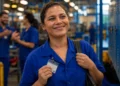 Trabalhadora de uniforme azul segura crachá em fábrica após anúncio de mudanças na jornada de trabalho com fim da escala 6x1.