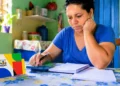 Mulher faz cálculos do orçamento doméstico diante de material do Bolsa Família, representando a manutenção do benefício em 2027.