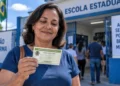Mulher segurando título de eleitor em frente a uma escola durante o dia de votação, ilustrando a validação da Prova de Vida do INSS pelo comparecimento às urnas.