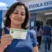 INSS confirma: comparecimento às urnas conta para a Prova de Vida automática 14 Mulher segurando título de eleitor em frente a uma escola durante o dia de votação, ilustrando a validação da Prova de Vida do INSS pelo comparecimento às urnas.