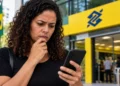 Mulher preocupada consulta o celular diante de agência bancária após anúncio do fim das bets no Brasil.