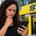 Bets chegam ao fim no Brasil: governo define datas para encerramento das apostas e retirada de valores 14 Mulher preocupada consulta o celular diante de agência bancária após anúncio do fim das bets no Brasil.