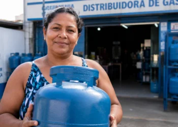 Beneficiária do Gás do Povo segura botijão em frente a uma revenda credenciada.