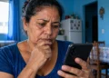 Beneficiária do INSS observa celular preocupada com mensagem falsa sobre prova de vida