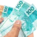 Notas de reais em mãos representando o pagamento dos benefícios do INSS de setembro para segurados