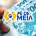 Mão segurando notas de dinheiro de R$ 100 com a marca do programa Pé-de-Meia ao centro da imagem.