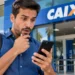Homem consulta celular em frente a uma agência da Caixa, representando o lançamento do Pix Parcelado pelo aplicativo.