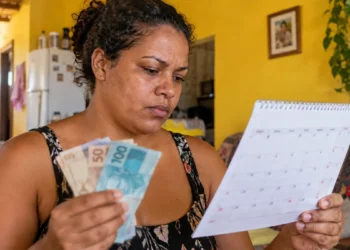 Mulher confere calendário e segura dinheiro, representando as próximas datas de pagamento do Mães de Pernambuco em 2026.