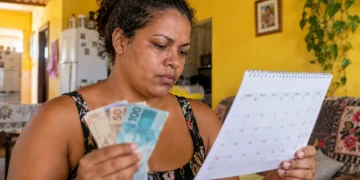 Mulher confere calendário e segura dinheiro, representando as próximas datas de pagamento do Mães de Pernambuco em 2026.