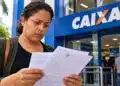 Bolsa Família cancelado na revisão pode ser revertido até seis meses após o corte; veja como regularizar 15 Mulher analisa documentos em frente à Caixa Econômica Federal, ilustrando a situação de famílias com Bolsa Família cancelado na revisão cadastral.