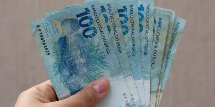 Mão segura notas de R$ 100, representando o valor que pode ser retirado pelo Saque Calamidade do FGTS por moradores de cidades que ainda estão habilitadas em outubro.