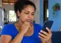Bolsa Família de outubro abre consulta no aplicativo nesta terça (6); veja como conferir o novo valor 14 Beneficiária consulta o celular em casa com expressão pensativa, representando a consulta ao Bolsa Família de outubro.