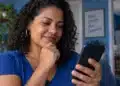 Abono PIS/Pasep: consulta no app deixa de mostrar “em processamento” antes do lote extra de quinta (15) 3 Mulher de blusa azul consulta informações pelo celular enquanto está sentada no sofá de casa.