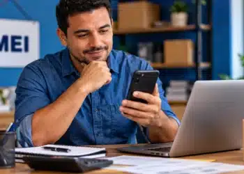 Governo entra em contato com MEIs por mensagem para tratar do perdão de dívidas tributárias; entenda 7 Empreendedor MEI consulta o celular, representando o contato do Governo por mensagem relacionado ao perdão de dívidas tributárias.
