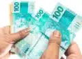 Portaria convoca bancos para a 3ª fase do Desenrola; prazo para enviar dívidas é de cinco dias úteis 14 Mãos segurando cédulas de R$ 100, em imagem que representa o prazo estabelecido para o envio de informações sobre dívidas bancárias à terceira fase do programa Desenrola.
