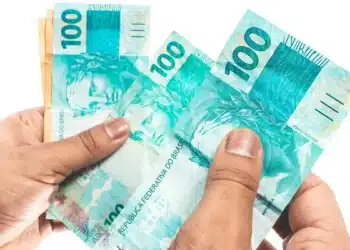 Portaria convoca bancos para a 3ª fase do Desenrola; prazo para enviar dívidas é de cinco dias úteis 5 Mãos segurando cédulas de R$ 100, em imagem que representa o prazo estabelecido para o envio de informações sobre dívidas bancárias à terceira fase do programa Desenrola.