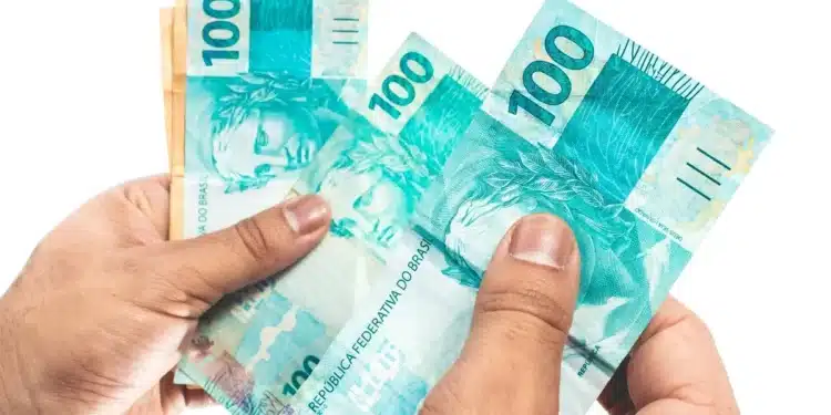 Portaria convoca bancos para a 3ª fase do Desenrola; prazo para enviar dívidas é de cinco dias úteis 1 Mãos segurando cédulas de R$ 100, em imagem que representa o prazo estabelecido para o envio de informações sobre dívidas bancárias à terceira fase do programa Desenrola.