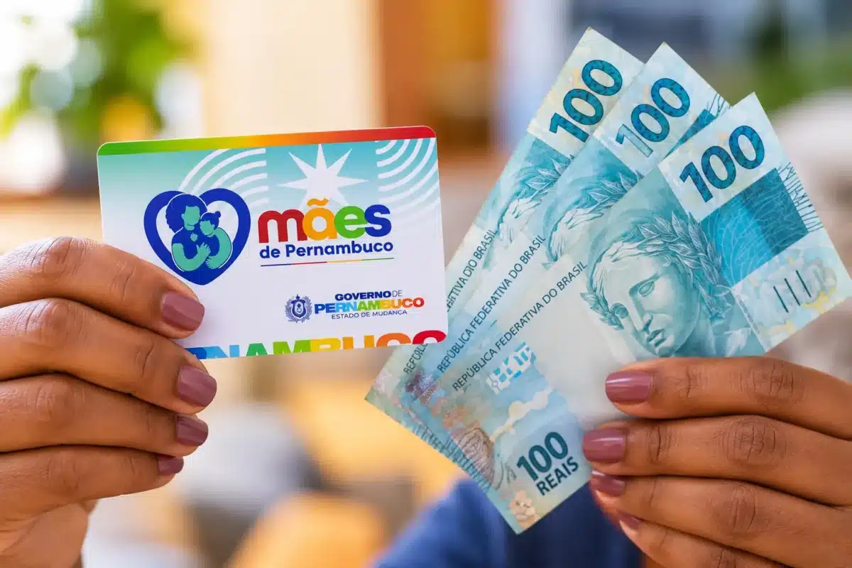 Mães de Pernambuco abre 2.760 vagas com auxílio de R$ 300 até 22 de outubro; veja quem pode se inscrever 2 Mãos seguram cartão do programa Mães de Pernambuco e três notas de R$ 100, ilustrando o benefício mensal e as condições para seu recebimento.