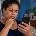 PixMEI ainda não tem repasse: ministro alerta para golpes com cadastros falsos do apoio de até R$ 5 mil 14 Mulher com expressão de preocupação observa a tela do celular em casa, ilustrando o alerta sobre golpes com cadastros falsos do PixMEI.