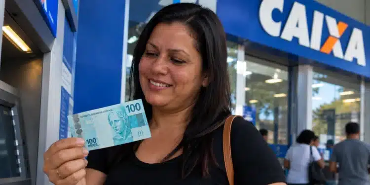 Mulher segura nota de R$ 100 em frente à Caixa, representando a liberação do saque-aniversário do FGTS para nascidos em novembro.