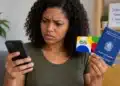 Mensagem sobre carteira de trabalho e Bolsa Família é falsa; veja o que o ministério esclareceu 14 Mulher com expressão de dúvida consulta mensagem no celular enquanto segura cartão do Bolsa Família e carteira de trabalho.