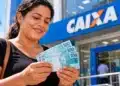 Caixa libera nesta segunda (26) novo pagamento de valores esquecidos do PIS/Pasep; veja quem recebe 4 Mulher segura notas de R$ 100 em frente a uma agência da Caixa, representando o novo pagamento de valores esquecidos do PIS/Pasep.
