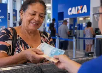 INSS paga BPC de outubro a partir do dia 26; benefício de R$ 1.621 sai conforme o final do cartão 7 Mulher recebe dinheiro em agência bancária, representando o pagamento do BPC de outubro pelo INSS.
