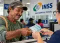 Pescador artesanal recebe cédulas de dinheiro durante atendimento em agência do INSS, representando o pagamento do último lote do Seguro-Defeso pelo Instituto.