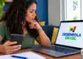 Desenrola Adimplentes está na reta final; veja quem pode renegociar e quem fica de fora do programa 15 Mulher consulta o programa Desenrola Brasil no notebook enquanto segura o celular.