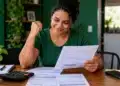 MEI com dívida de até R$ 8.105 pode parcelar em até 60 meses com desconto de 50%; veja como aderir 14 Mulher analisa boletos e documentos financeiros em casa, representando a possibilidade de renegociação de dívidas para microempreendedores individuais.