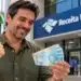 Restituição antecipada: Receita Federal já pagou R$ 41 bilhões a 25,9 milhões de contribuintes 14 Homem segura cédulas de R$ 100 em frente à Receita Federal, ilustrando a restituição antecipada do Imposto de Renda.